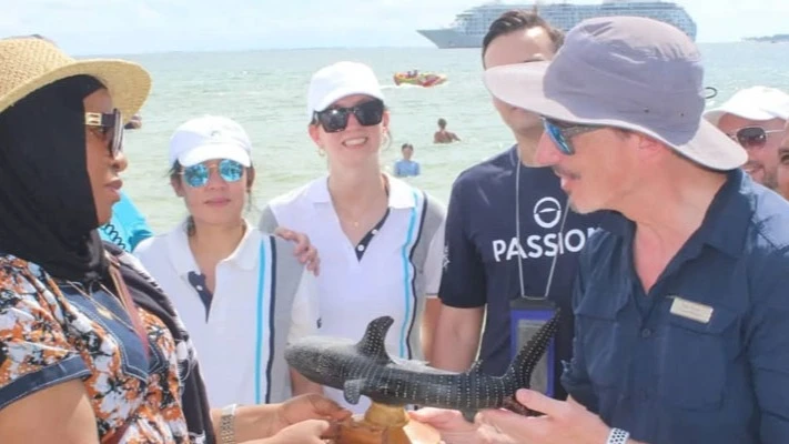 Mafia district commissioner Aziza Mangosongo (L) pictured yesterday presenting a souvenir shark sculpture to one of the crew members of private residential cruise ship MS The World, now anchored on Mafia Island with foreign tourists on board. 