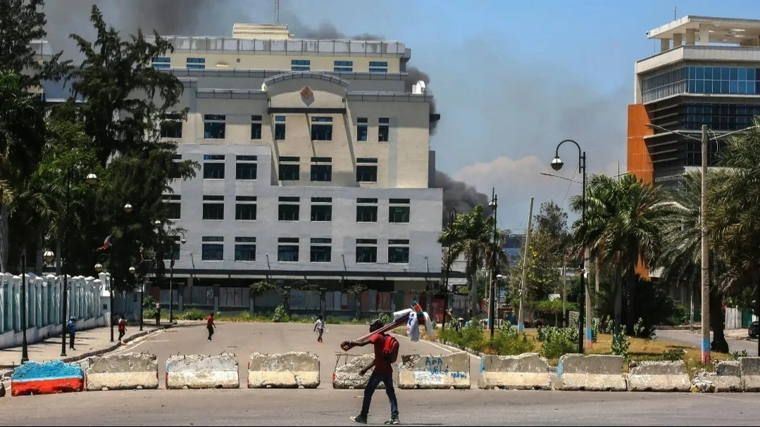 As smoke billows from the Ministry of Finance building behind them, people leave the area after hearing gunshots from armed gangs near the National Palace in Port-au-Prince, Haiti, on April 2, 2024.