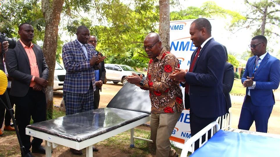 Former Missenyi District Commissioner, Col. Wilson Sakulo (3rd R) claps hands after receiving hospital beds and one examination bed for Luzinga Dispensary in the district from the then NMB Bank’s Acting Lake Zone Manager, Dickson Richard during a handover
