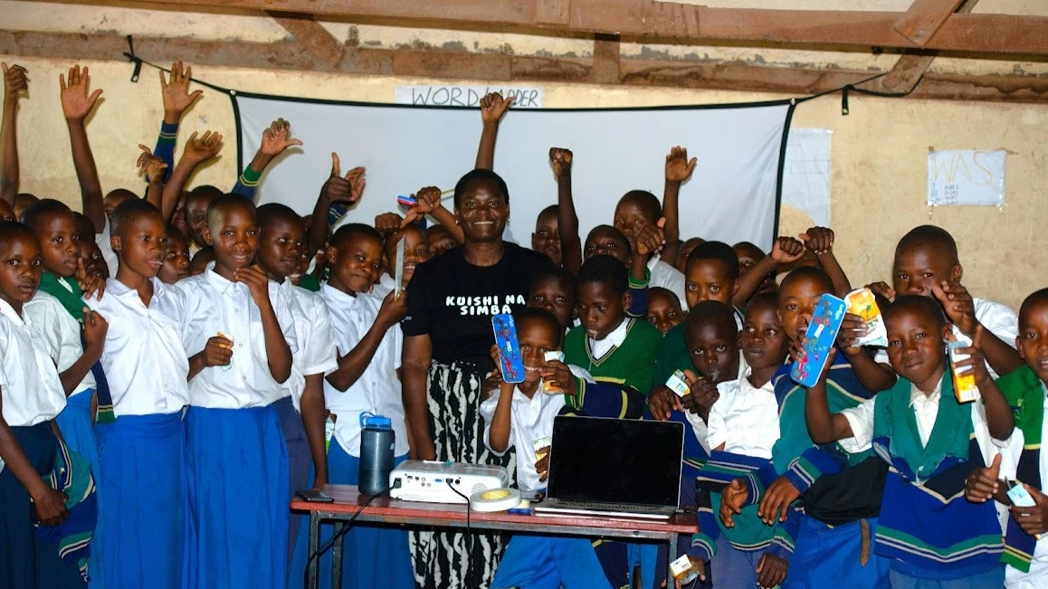 Tanzania female nature and wildlife filmmaker, Erica Rugabandana in a group photo with pupils at one of the schools near Serengeti National Park soon after training and screening of a special film on how to live with lions.