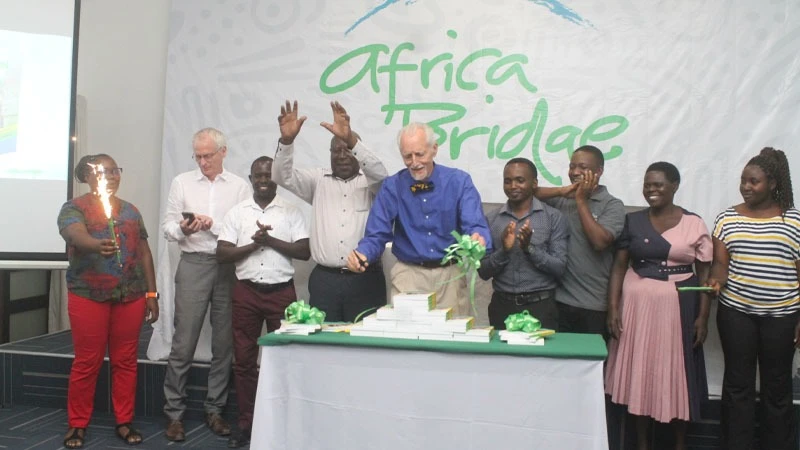 The author of the book titled “And the Children Shall Lead Us”Barry Childs (C) cuts a ribbon to officiate the launching of the book on his left is co-author Philip Whiteley and other are officials from Africa Bridge project and stakeholders.