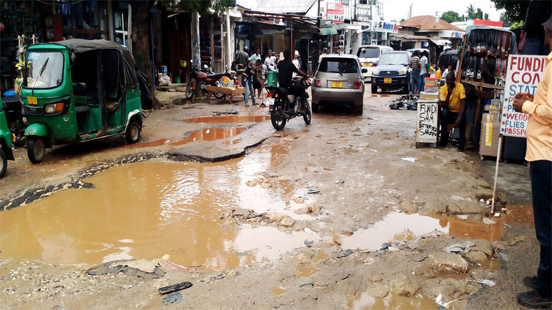 Drivers of cars and motorcycles negotiate their way on the damaged road at the sparkling shopping area at Mwenge in Kinondoni municipality, Dar es Salaam yesterday, posing plenty of inconvenience to traders and customers interacting in the area. 